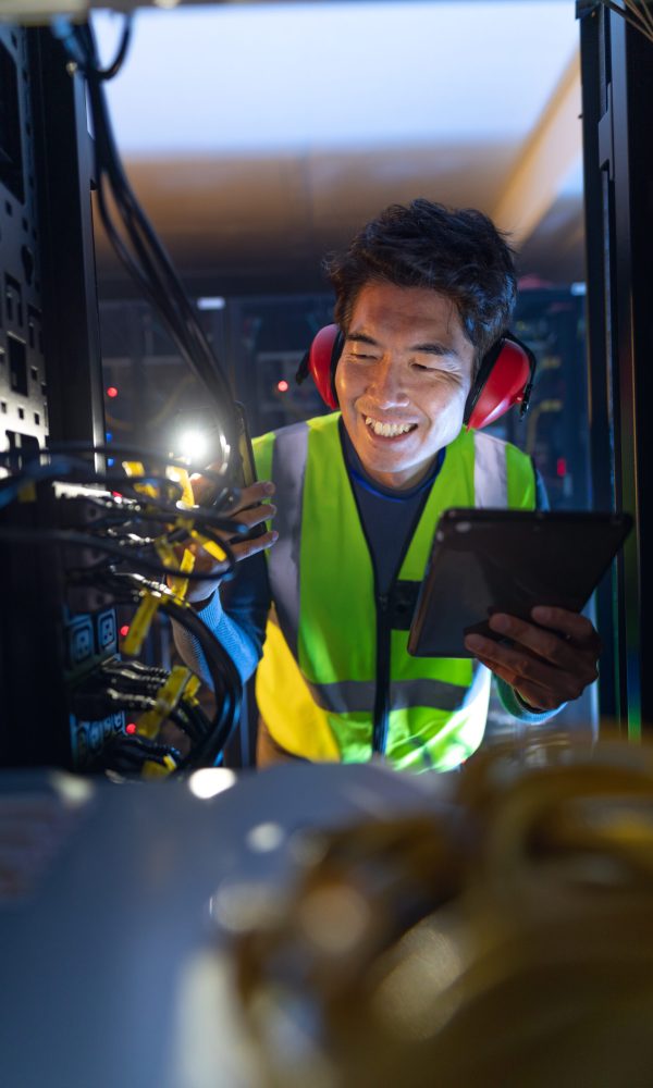 Asian male engineer using smartphone flash while inspecting the server in computer server room. database server management and maintenance concept